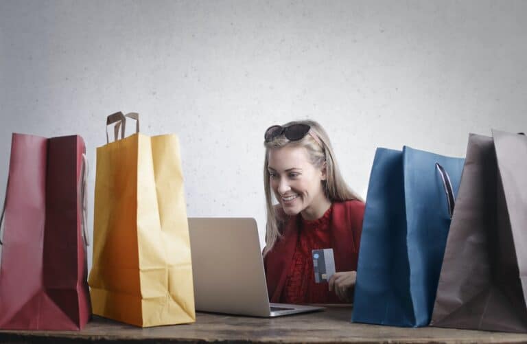 A woman sitting at a table with shopping bags and a laptop, enjoying positive reviews.