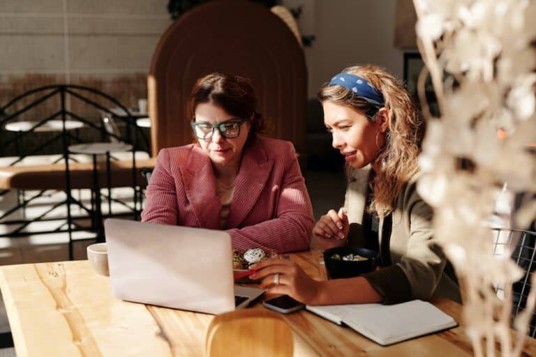 Two women conducting a marketing review while sitting at a table with a laptop.