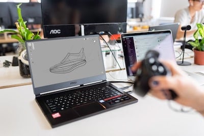 A person is using a computer to draw a shoe on a laptop.