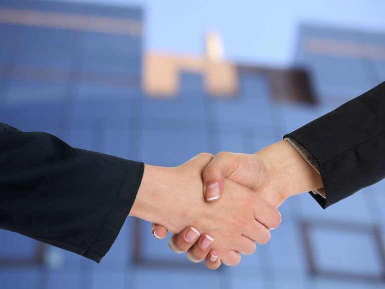 Two business people building trust and authenticity by shaking hands in front of a building.
