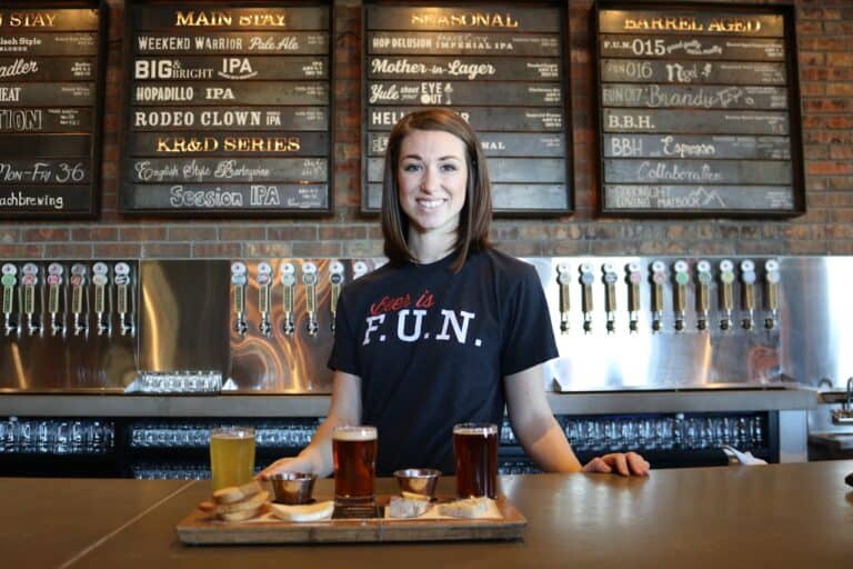 A woman utilizing review management software stands behind a bar with beer on a tray.