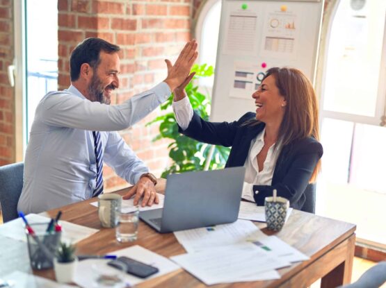 Two business people celebrating their successful online reputation with high fives in an office.