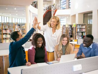 A group of people using online review software in a library giving each other high fives.